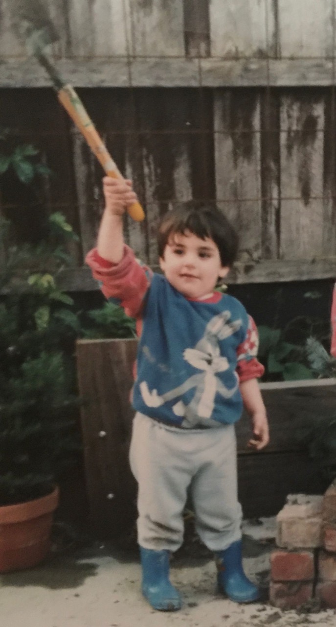 Matthew as a child, holding a tool above his head and wearing blue gumboots.